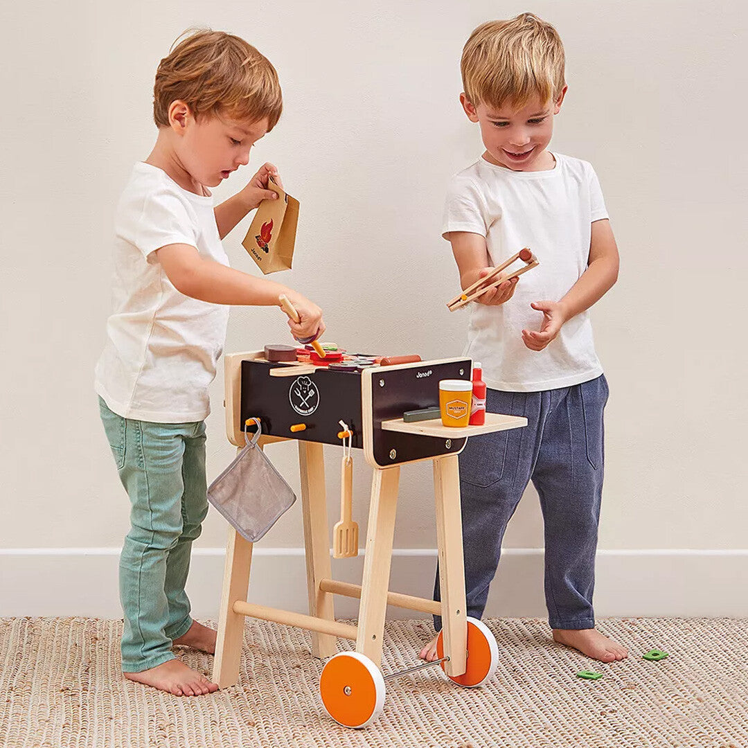 Twee jongens spelen met de Janod houten kinderbarbecue en de bijbehorende speelgoedingrediënten.