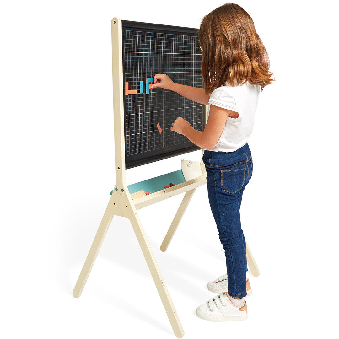 Een kind plaatst gekleurde geometrische vormen op het Janod houten schoolbord.