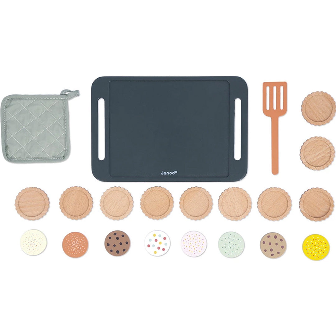 Alle onderdelen van de Janod houten koekjes bakken speelset, inclusief bakplaat, ovenwant, spatel en losse koekjes met toppings, van bovenaf gezien.