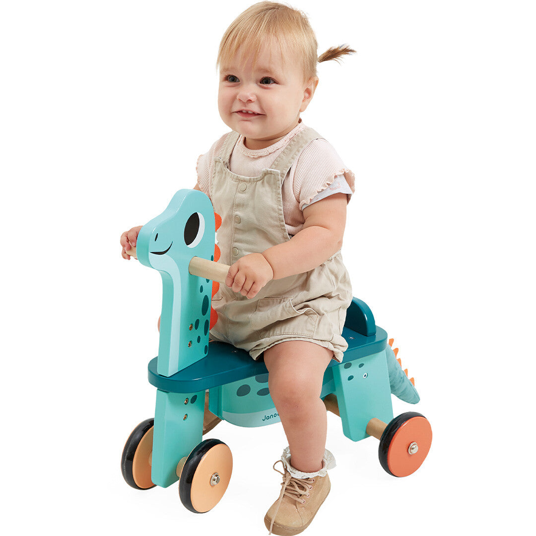 Een lachende baby zit op de Janod houten loopfiets Portosaurus.