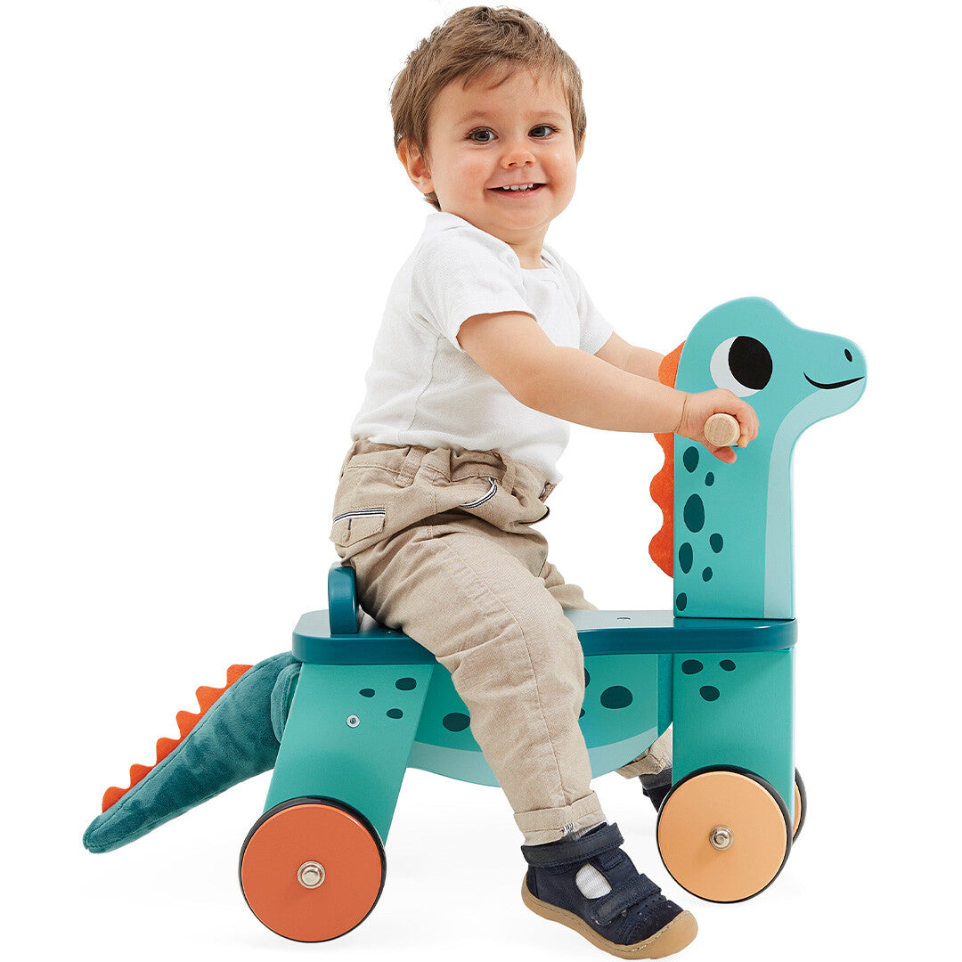 Een lachende peuter zit op de Janod houten loopfiets Portosaurus.