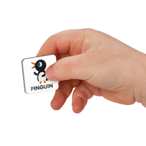Een kinderhand houdt een Janod magnetische tegel vast met een pinguïn en de tekst 'Pinguin'.