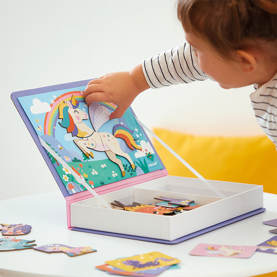 Een kind plaatst een eenhoorn magneetstuk op het Janod magneetboek met een regenboogachtergrond.