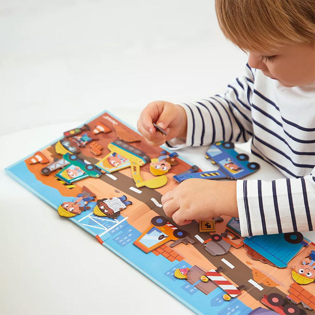 Een kind speelt met het Janod Magnéti'stories magneetboek bouwterrein, magneten op de speelmat plaatsend.