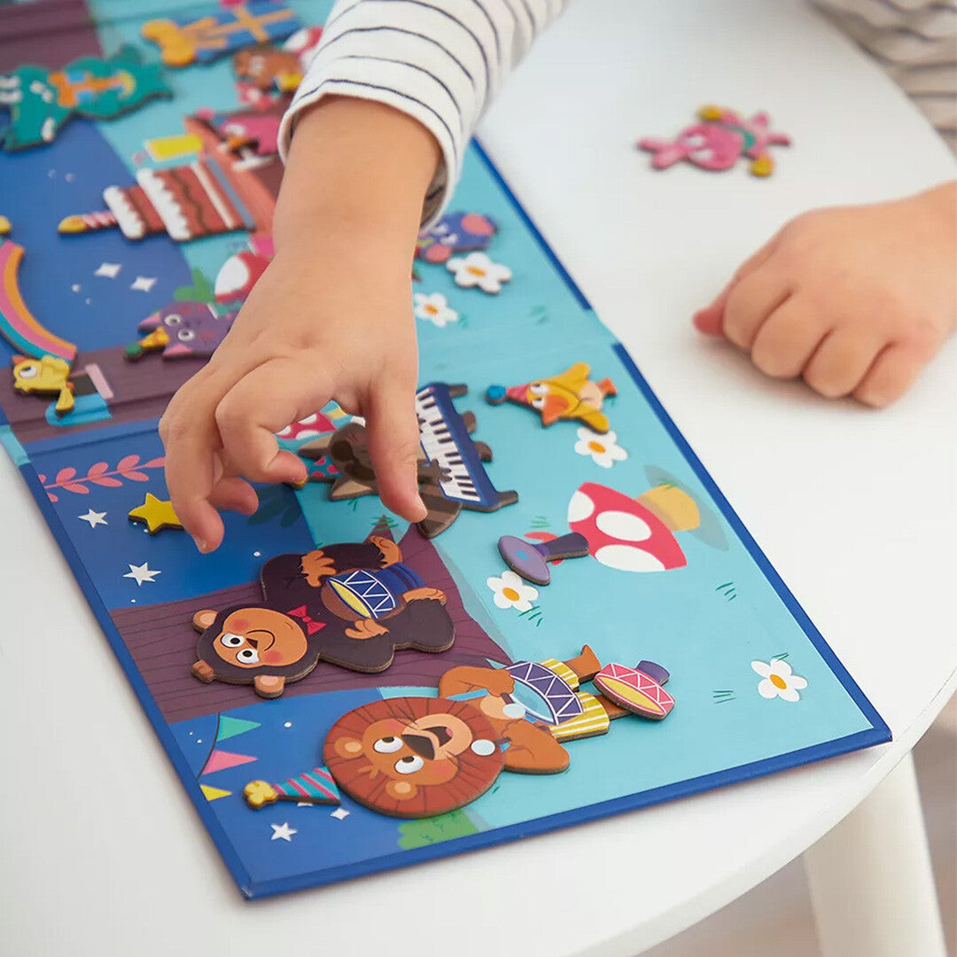Kinderhanden plaatsen magnetische dierenfiguren op het Janod magnetische speelbord met een bosscène.