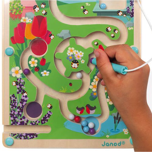 Een kinderhand gebruikt de magnetische pen om een kraal door het Janod magnetisch doolhof bijenkorf met tuinthema te leiden.
