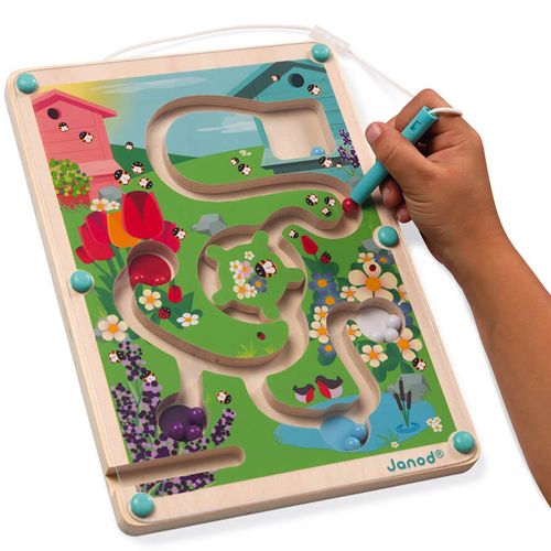 Een kinderhand leidt een kraal door het Janod magnetisch doolhof bijenkorf met tuinthema, schuin gefotografeerd.