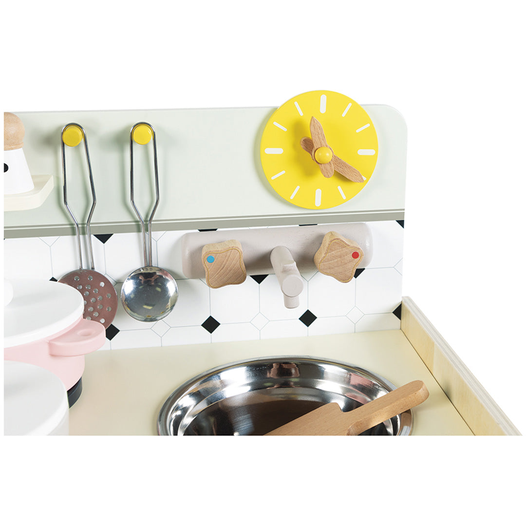 Detail van de Janod mini speelgoedkeuken met de gootsteen, kraan, gele klok en hangende keukenhulpjes.