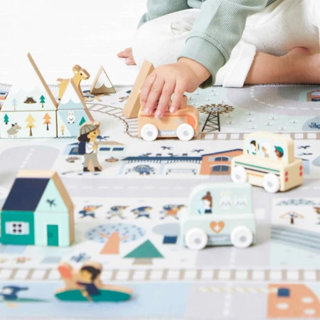 Kind speelt met houten speelgoedvoertuigen en accessoires op een speelmat.