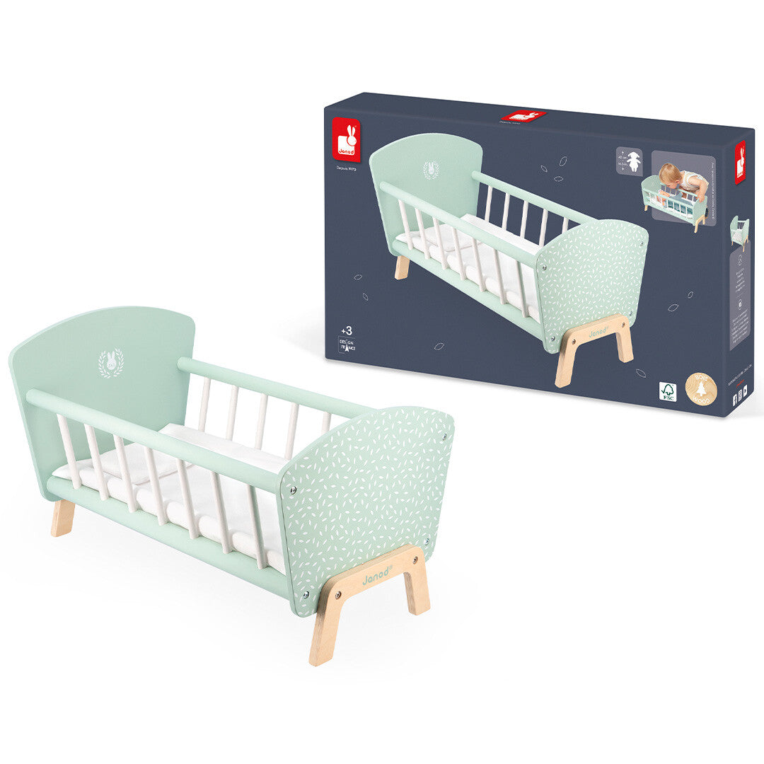 Het Janod poppenbed staat naast de donkerblauwe productverpakking.