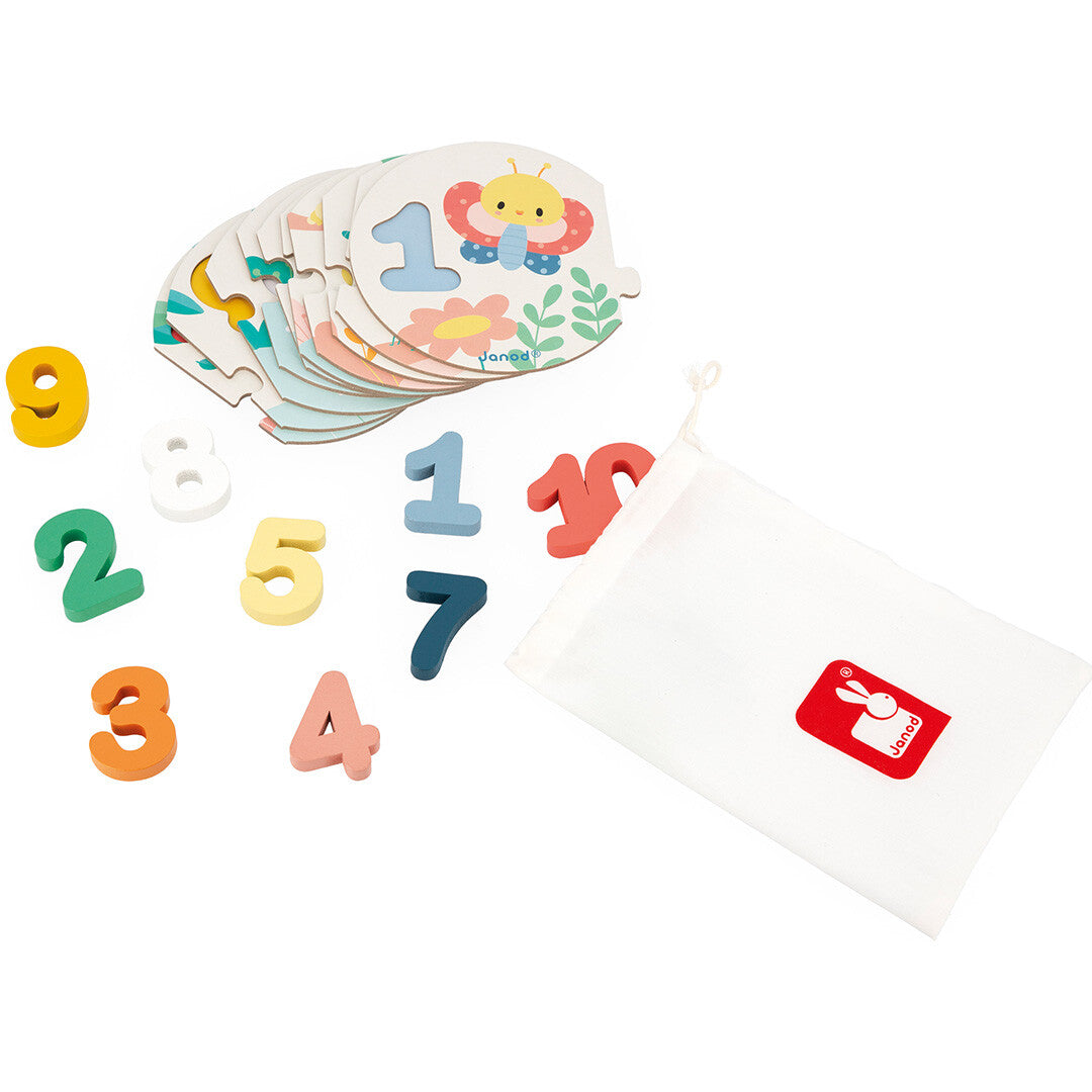Losse houten cijferpuzzelstukken en de bijbehorende houten cijfers, naast een wit katoenen Janod opbergzakje.