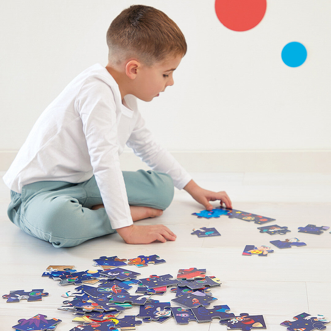 Een kind zit op de grond en kijkt naar de losse stukjes van de Janod legpuzzel met ruimte thema.