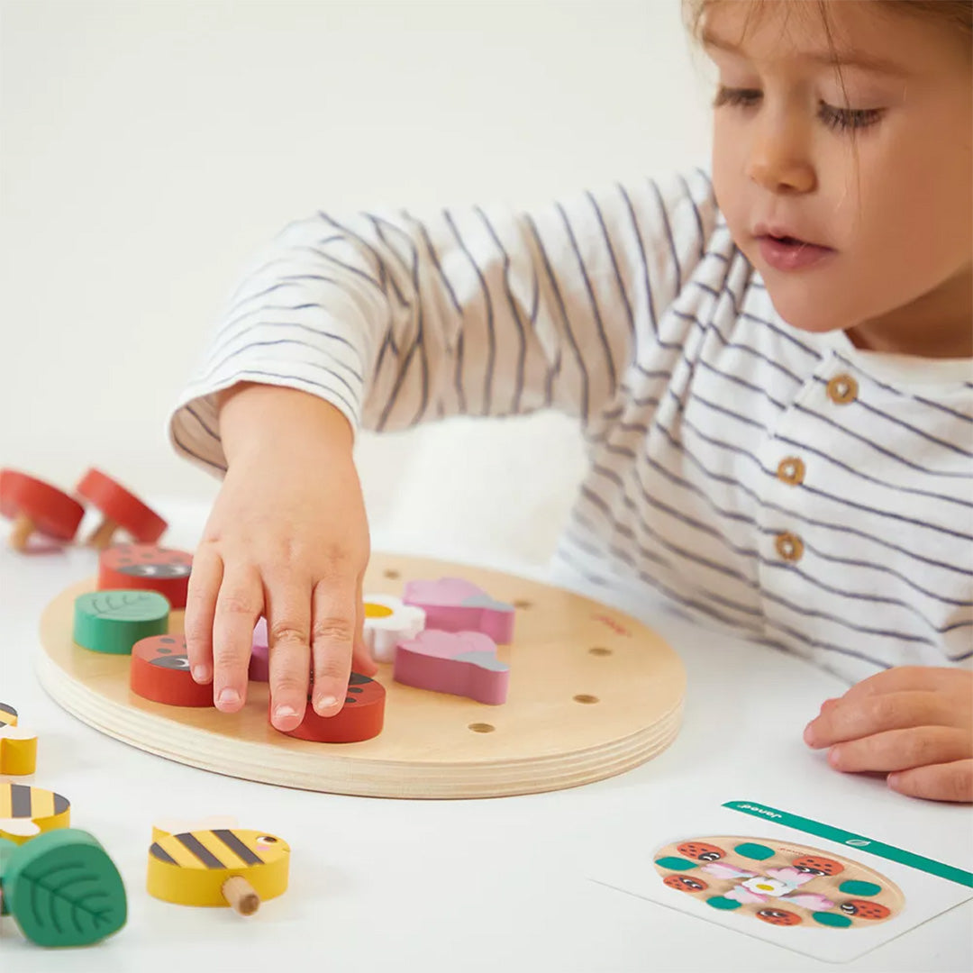 Een kind speelt met het Janod houten mandala puzzelspel met lieveheersbeestjes en bloemen.