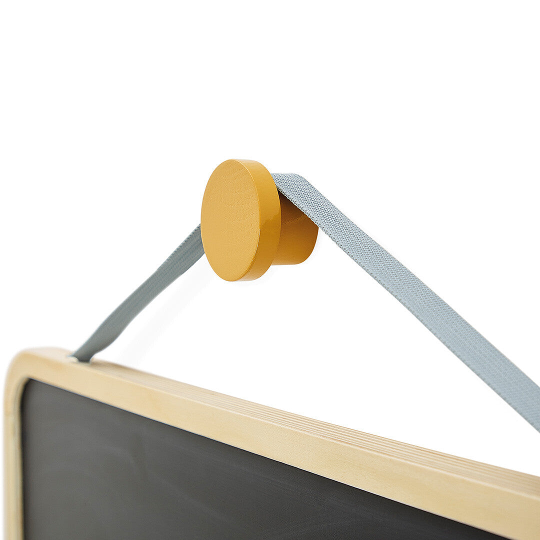 Detail van de gele houten knop en de grijze ophangband van het Janod schoolbord.