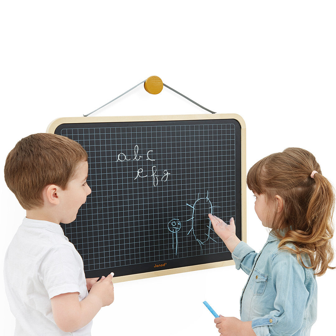 Twee kinderen tekenen op het Janod hangende schoolbord met ruitjespatroon.