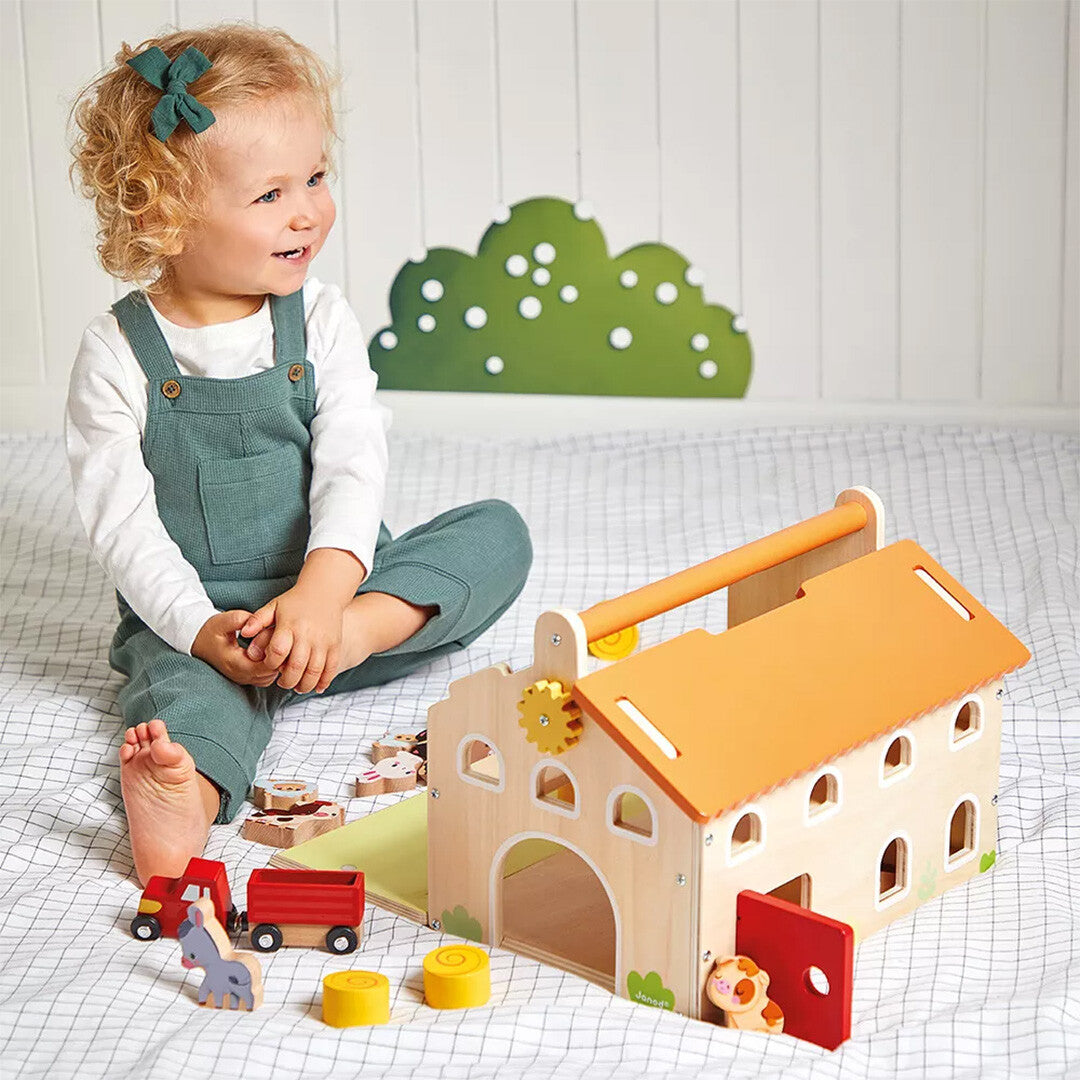 Een lachende peuter speelt op een deken met de Janod houten boerderij speelset en de bijbehorende dieren.