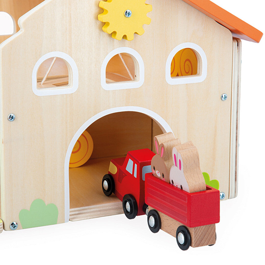 Detail van de Janod houten boerderij speelset met een rood vrachtwagentje met twee konijnen dat de boerderij inrijdt.
