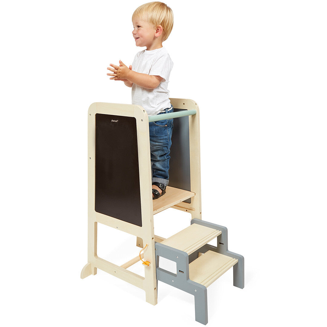 Een peuter staat op de Janod houten uitkijkpost met schoolbord en klapt in zijn handen.