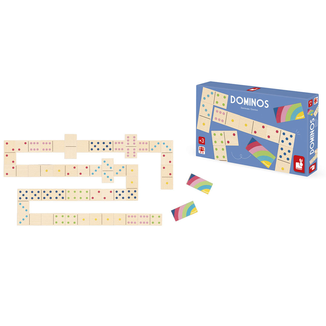 Janod houten dominostenen met gekleurde punten in een speelopstelling, naast de Janod domino spelverpakking en twee regenboogkaarten.