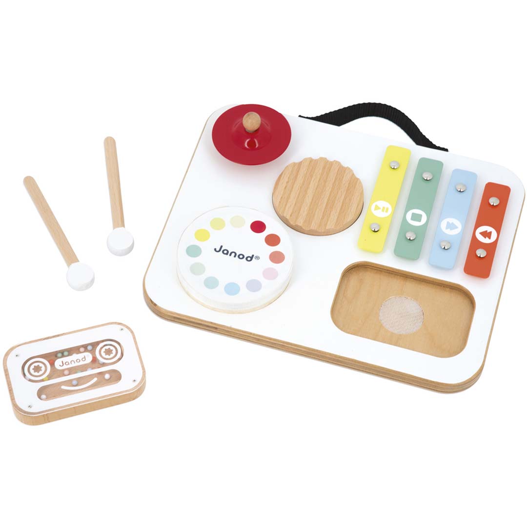 De Janod muziektafel confetti, een wit houten babyspeelgoed met xylofoon, cymbaal en draaischijf, met de losse cassette shaker en drumstokjes ernaast.