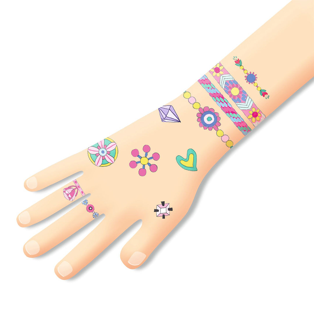 Een hand met diverse tijdelijke tattoos van sieraden, bloemen, een hart en een diamant.