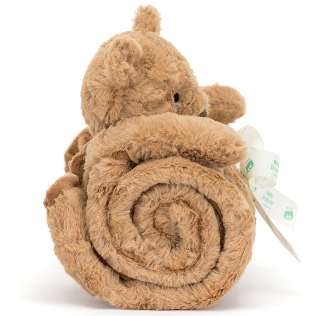 Zijaanzicht van het Jellycat knuffeldekentje, opgerold met de bruine pluchen beer erbovenop en een wit lint eromheen.