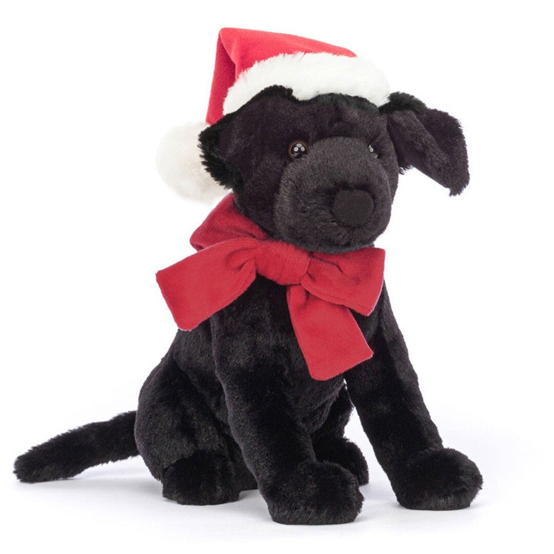 Jellycat knuffelhond Pippa, een zwarte pluchen hond met rode kerstmuts en rode strik, zit schuin van voren.