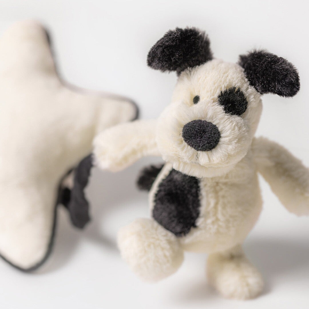 Close-up van de Jellycat pluchen puppy met zwarte vlekken, staand voor een wazige ster.