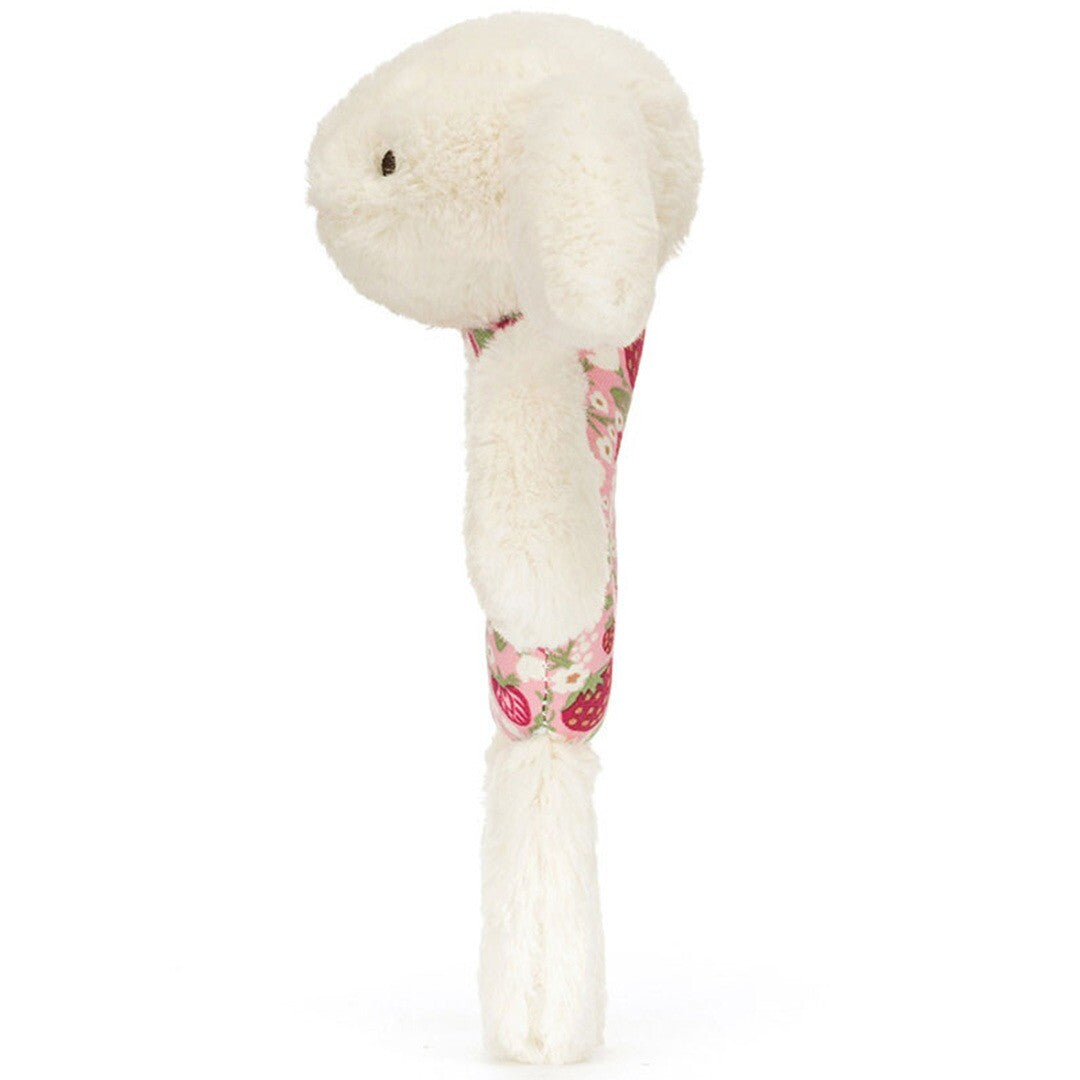 Zijaanzicht van de Jellycat babyspeelgoed rammelaar, een crème konijn met roze bloemen- en aardbeienpatroon.