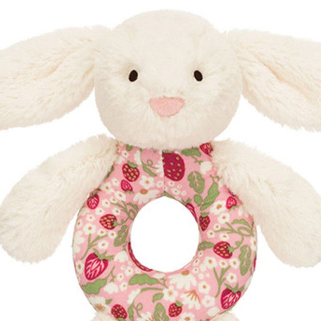 Detailopname van de kop en buik van de Jellycat babyspeelgoed rammelaar, een crème konijn met roze bloemen- en aardbeienpatroon.