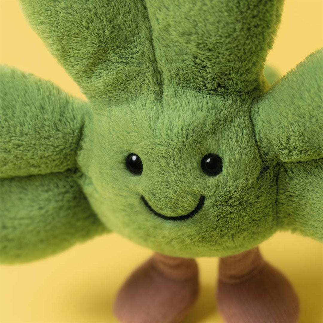 Close-up van het lachende gezicht van het groene pluchen klavertje met bruine voetjes, op een gele achtergrond.
