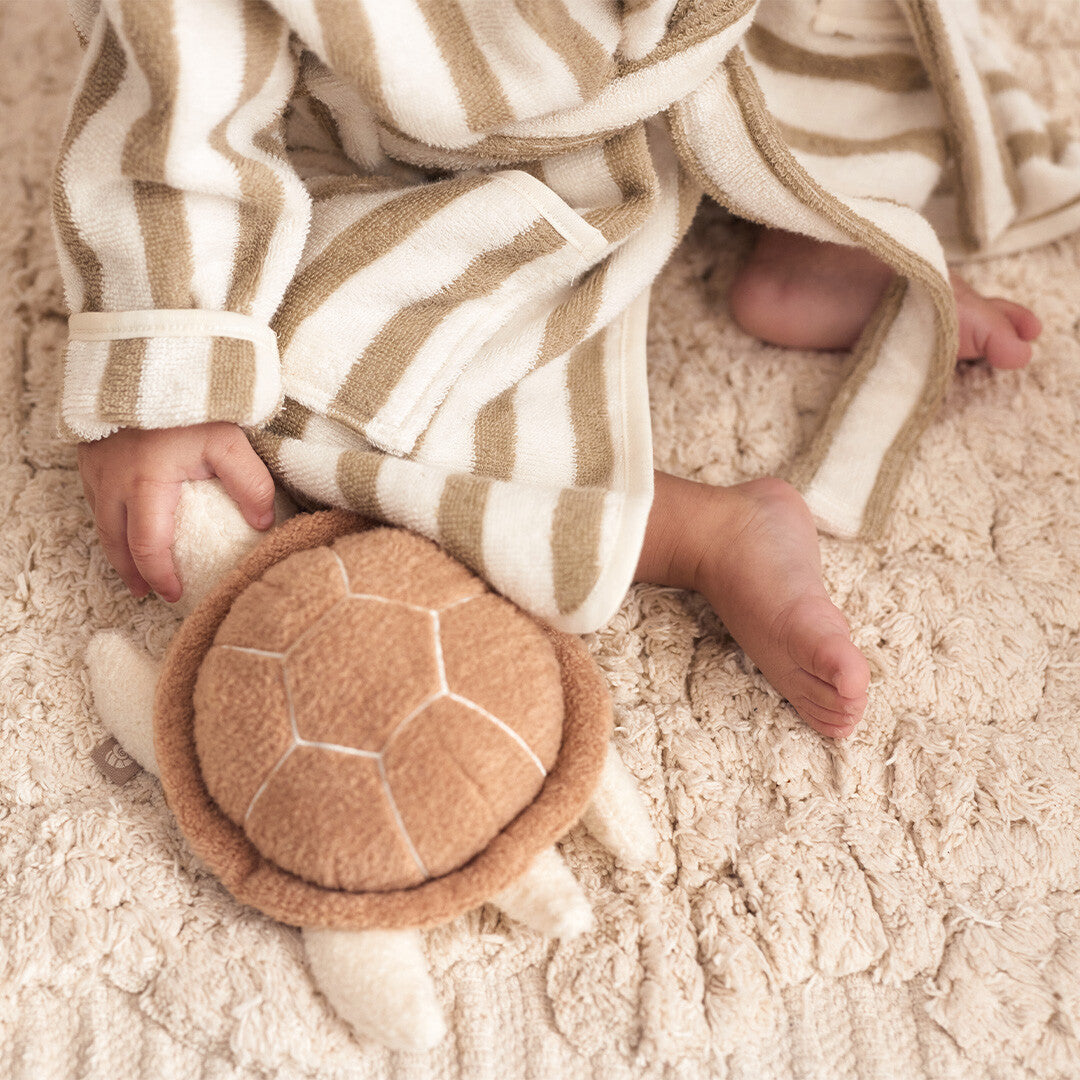 Een baby ligt met de Jollein activiteitenknuffel schildpad op een zachte, crèmekleurige deken.