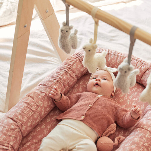 Baby ligt in een babynest onder de Jollein babygym met hangende lama speeltjes.