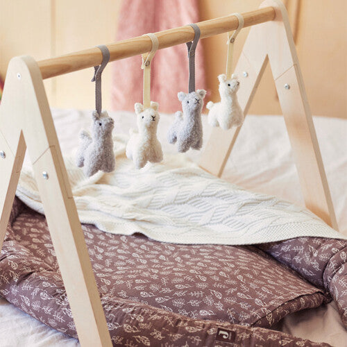 Jollein houten babygym met vier hangende lama speeltjes boven een babynest.