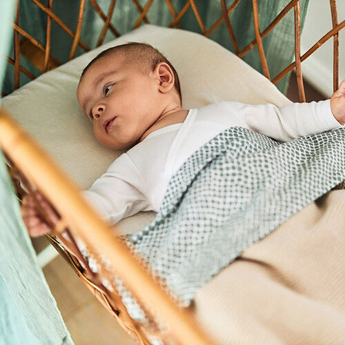 Baby ligt in een wieg op een jollein babyhoeslaken in nougat kleur.