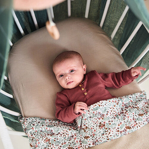 Baby ligt in een wieg op een jollein babyhoeslaken in nougat kleur.