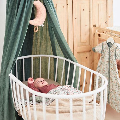 Baby ligt in een witte wieg met een jollein babyhoeslaken in nougat kleur.