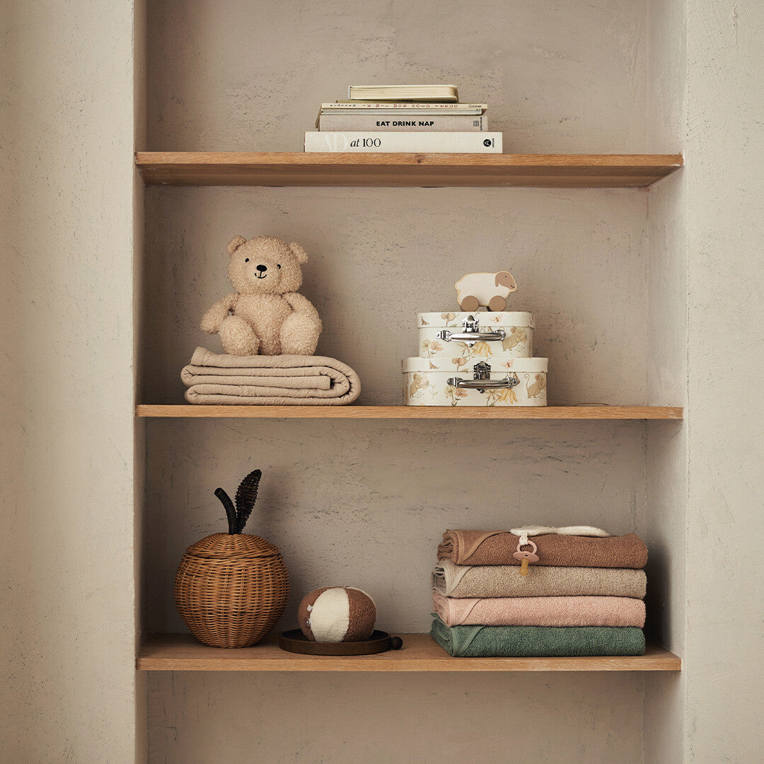 Een houten plank met diverse babyartikelen, waaronder een stapel Jollein badcapes en een teddybeer.