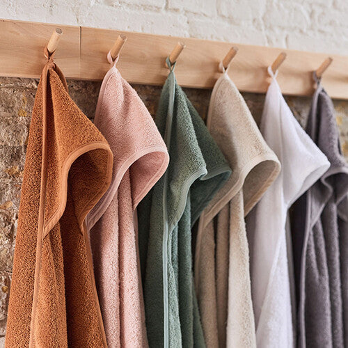 Detail van Jollein badcapes in verschillende kleuren hangend aan een houten rek.