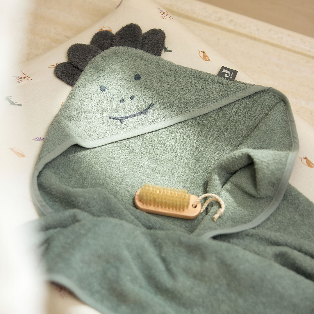 Jollein baby badcape met krokodillenhoofdje en een houten babyborstel op een patroonondergrond.
