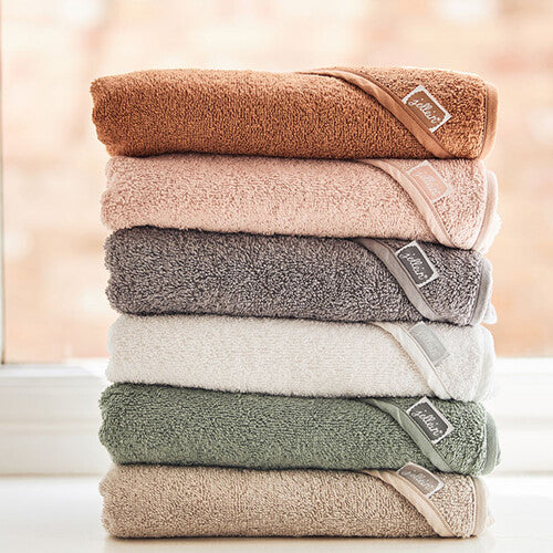 Een stapel Jollein badcapes in verschillende kleuren, elk met een merklabel, ligt op een vensterbank.