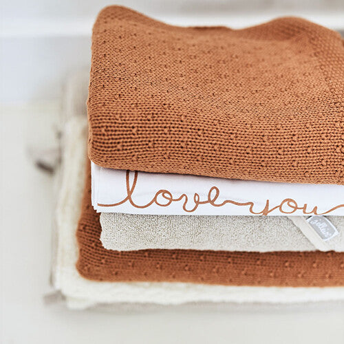 Een stapel babytextiel met een bruine deken, een witte doek en een Jollein badcape in nougat kleur.