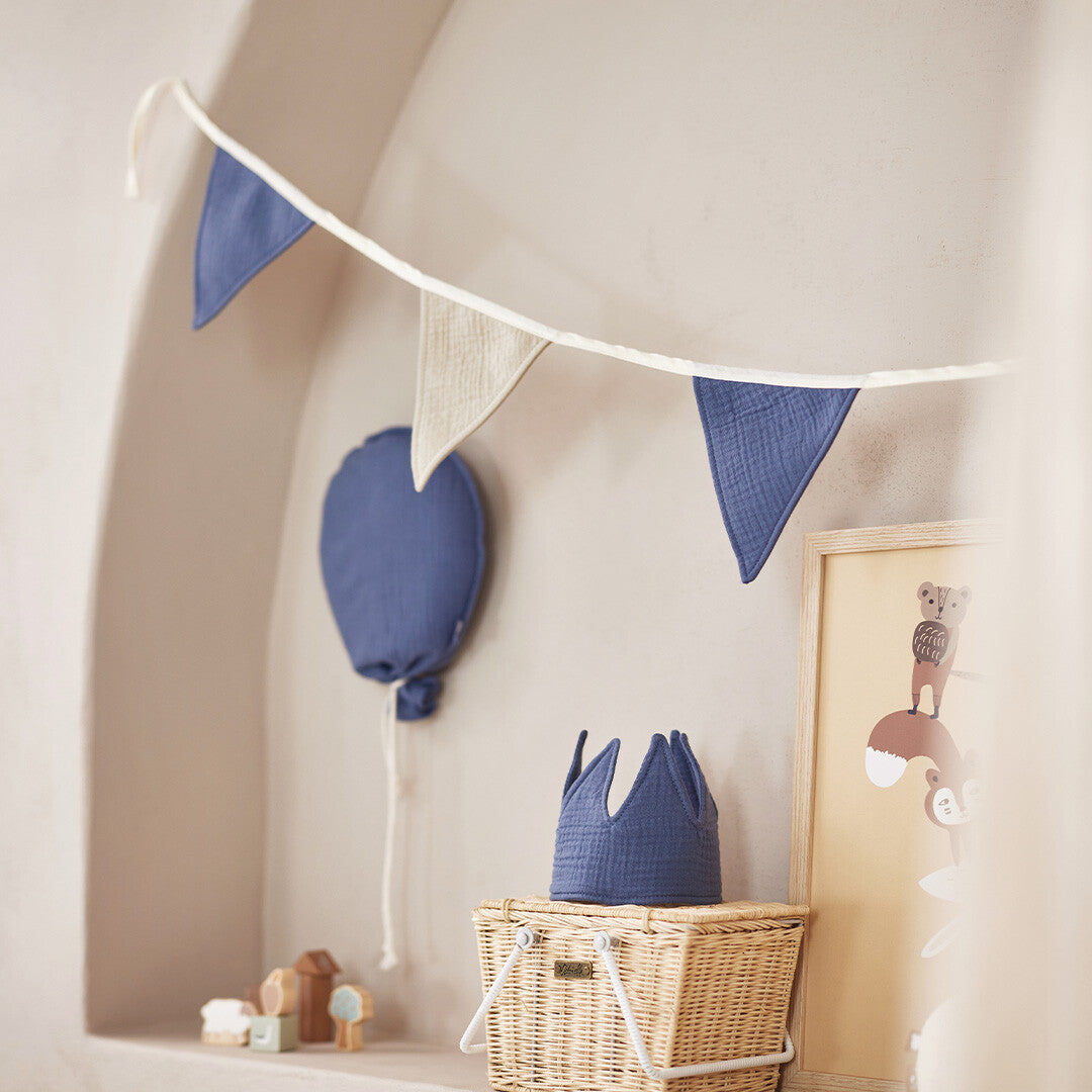 Jollein blauwe stoffen decoratieballon hangt aan een muur in een kinderkamer, met een vlaggenlijn erboven en een stoffen kroon op een mand.
