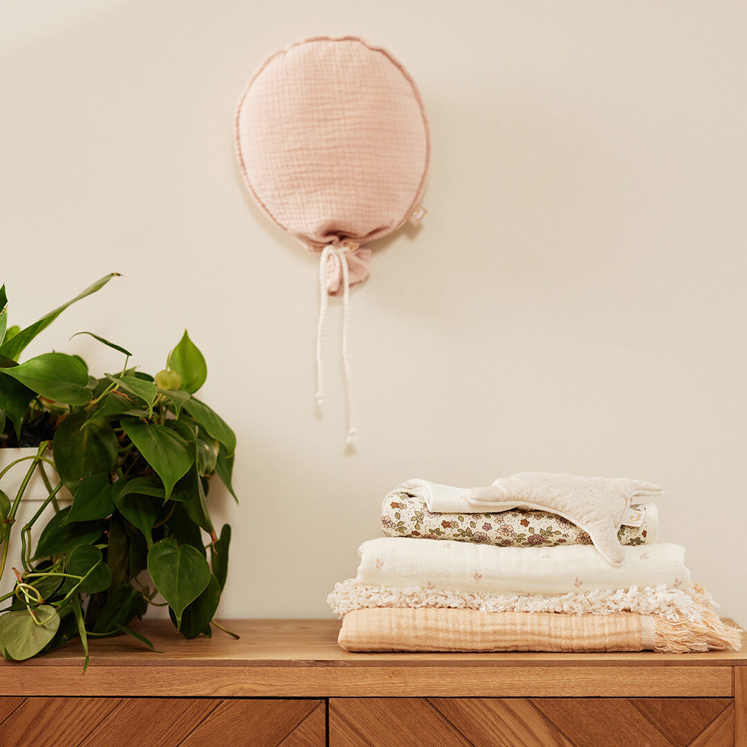 Jollein roze ballon decoratie hangend aan een muur boven een houten dressoir met plant.