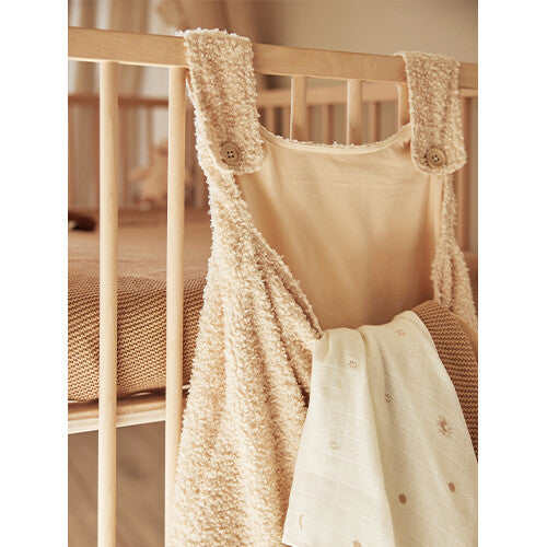 Jollein bouclé boxopbergzak in naturel kleur hangend aan een houten babybedje, gevuld met een wit babydekentje.