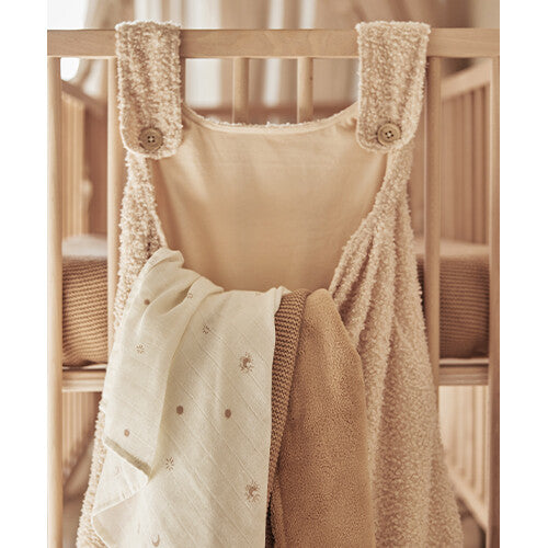 Jollein bouclé boxopbergzak in naturel kleur hangend aan een houten babybedje, gevuld met twee babydekens.