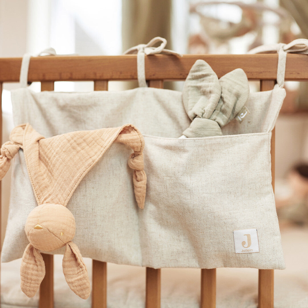Jollein boxopbergzak van beige katoen en linnen hangend aan een houten ledikant met knuffels.