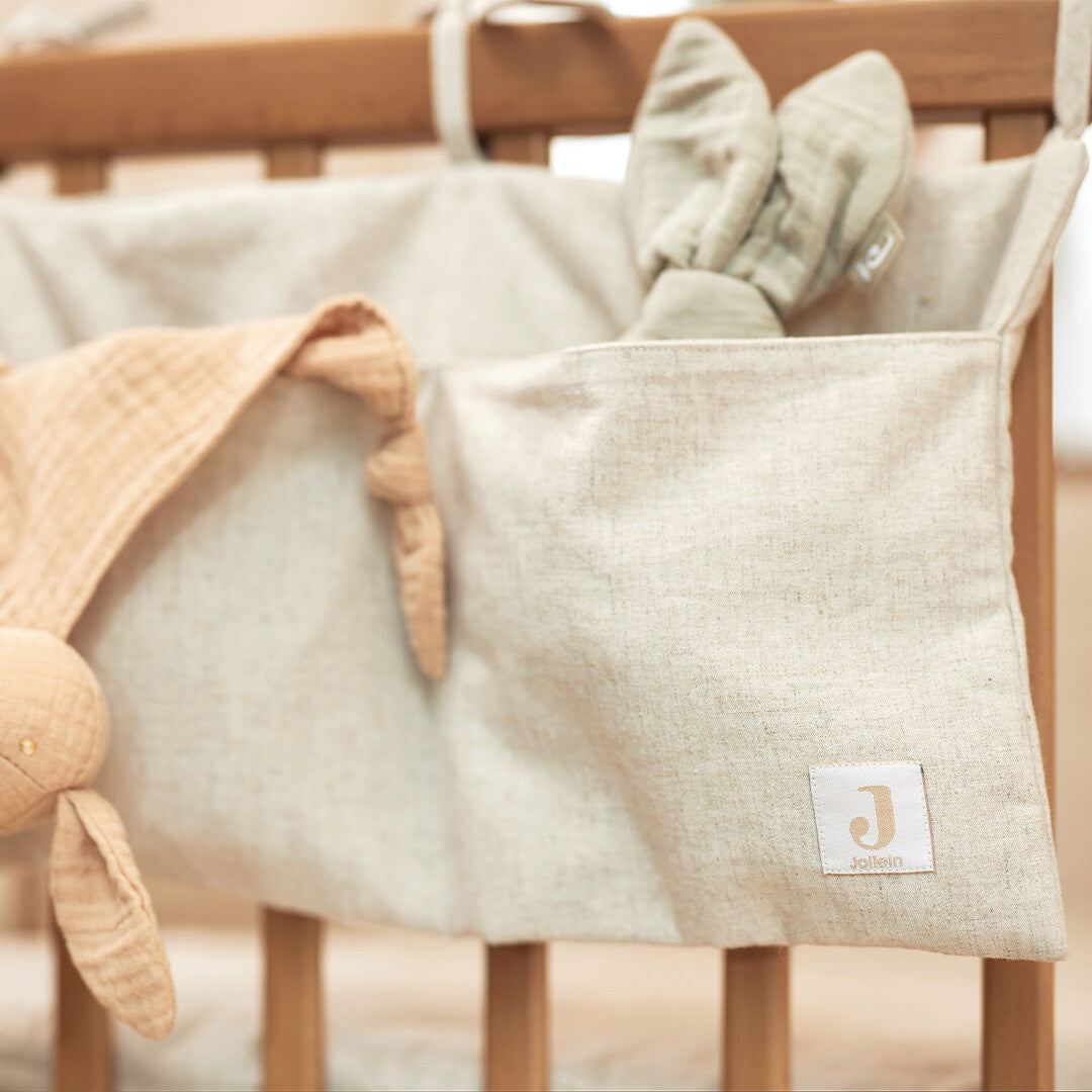 Jollein boxopbergzak van beige katoen en linnen hangend aan een houten ledikant met knuffels.