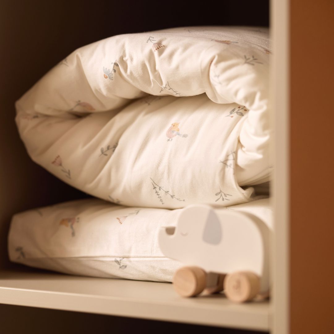 Jollein houten duwfiguur olifant staat op een plank naast opgevouwen babybeddengoed.