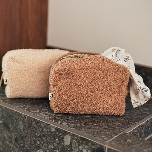 Twee Jollein bouclé toilettassen, één in biscuit en één in lichtbeige, staan naast elkaar op een donkere ondergrond.